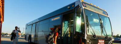 Student boards grey and red UL Lafayette bus, another student walking up from behind